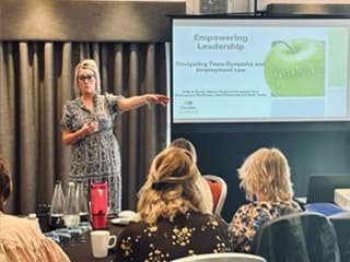 A woman presents a slideshow titled "Empowering Leadership" to an audience in a conference room.