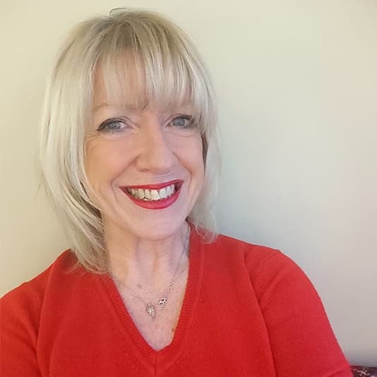 Smiling woman with shoulder-length blonde hair in a red sweater against a plain background.