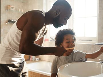 Father helping to brush his son's teeth at the bathroom sink