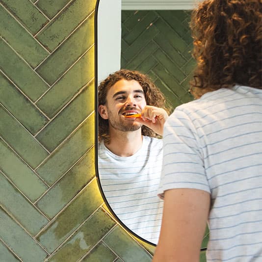 Man brushing teeth in bathroom mirror