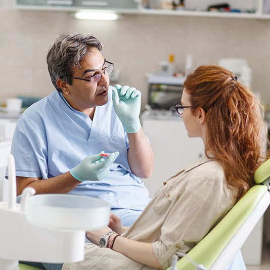 A professional dentist, equipped with a bright smile, converses with his red-haired female patient, carefully explaining the upcoming treatment, and ensuring her comfort throughout the process