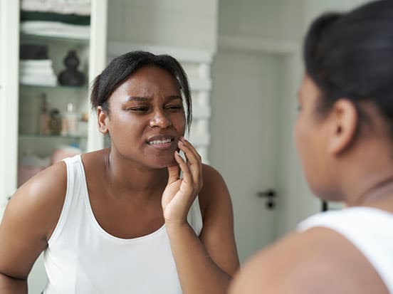 African lady with toothache in bathroom mirror
